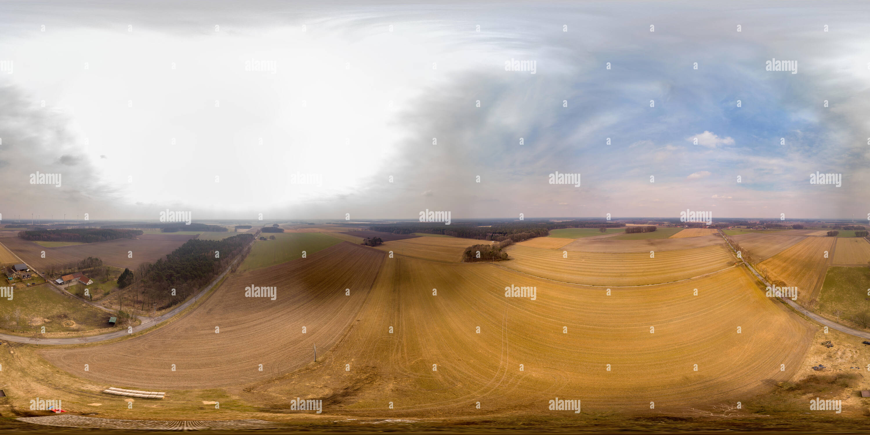 360 degree panoramic view of 360-degree overview of a harvested field in the lowlands of northern Germany with a farm in the background and windmills on the horizon.