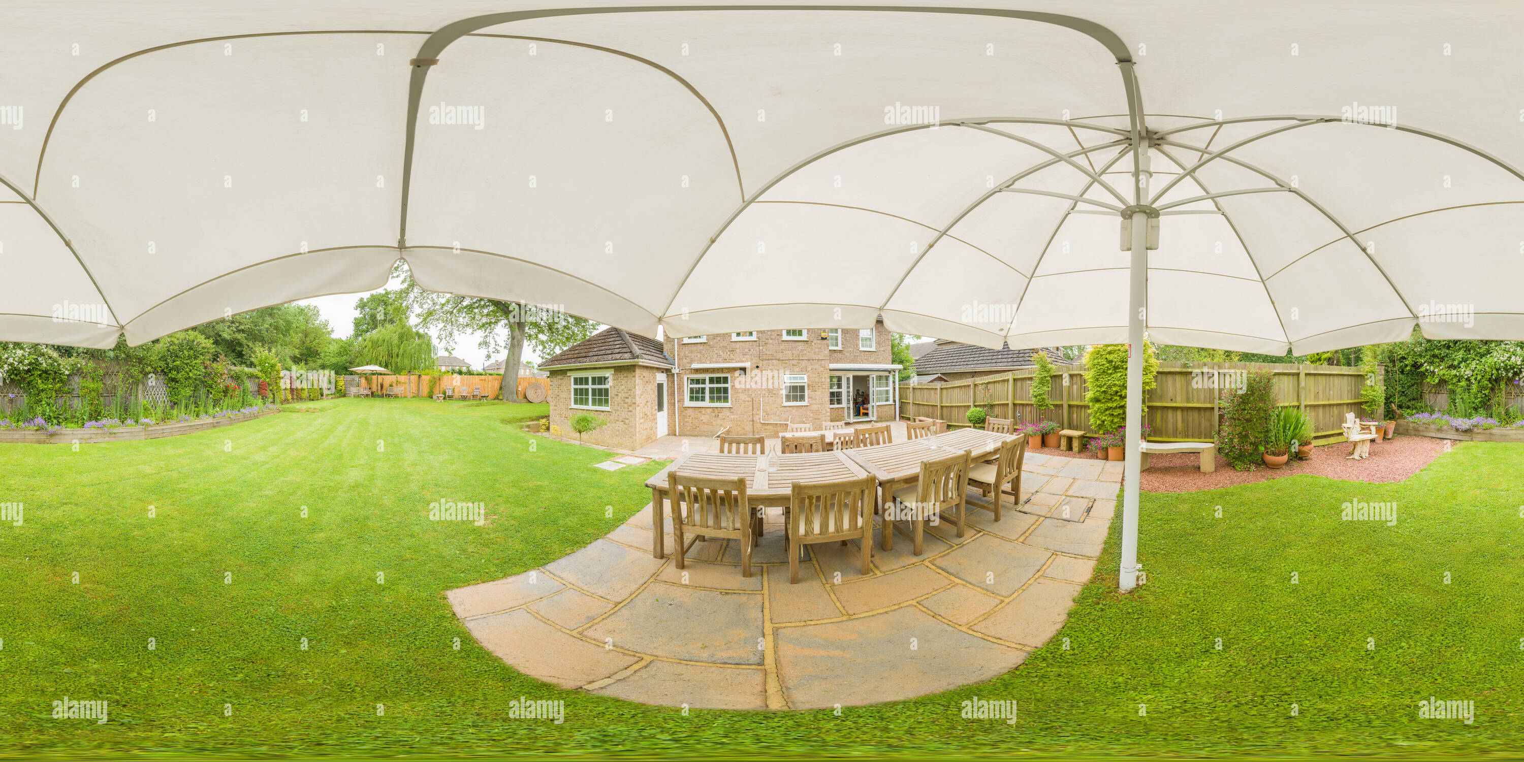 360 Grad Panorama Ansicht von Sonnenschirm über einem terrassenförmig angelegten Terrasse in den Garten eines englischen Home an einem Sommertag.